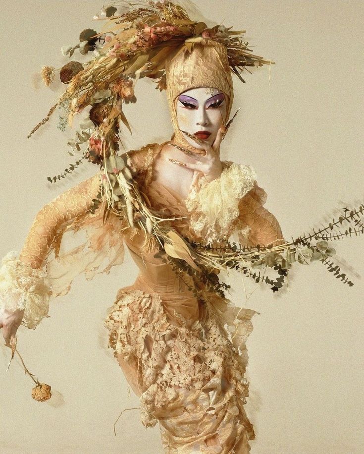 a woman dressed in costume with feathers and flowers on her head, holding a branch