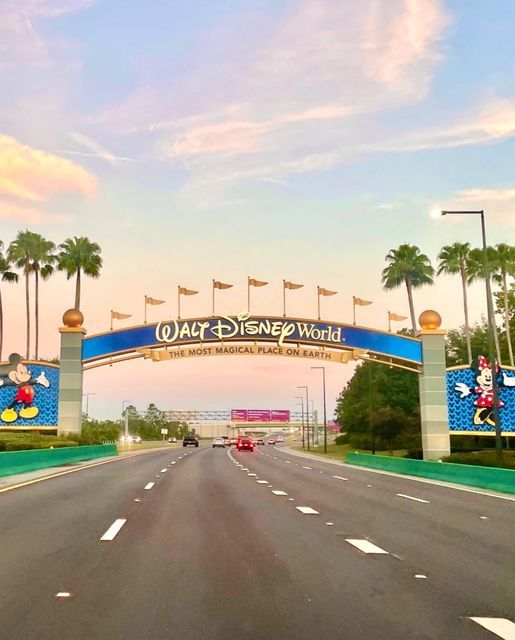 the entrance to walt world with cars driving under it and palm trees in the background