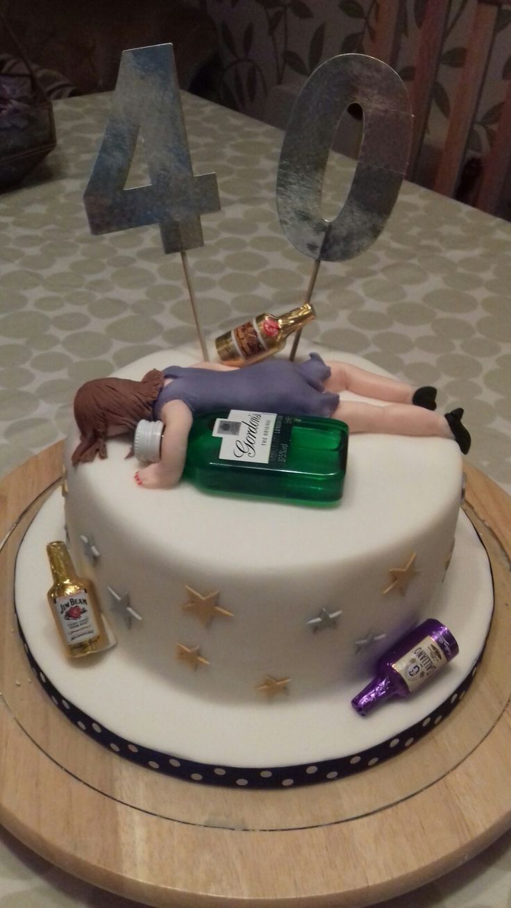 a woman laying on top of a table next to a cake with candles and bottles