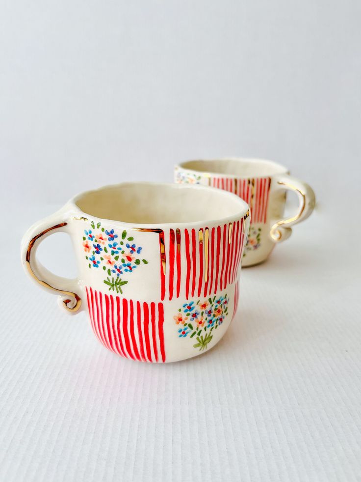 two red and white cups with flowers on them sitting next to each other in front of a white background