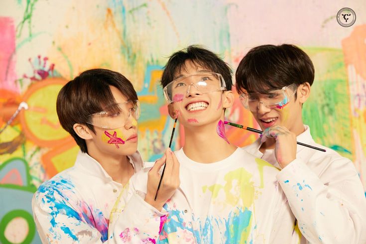 three young men with face paint on their faces posing for a photo in front of a colorful wall