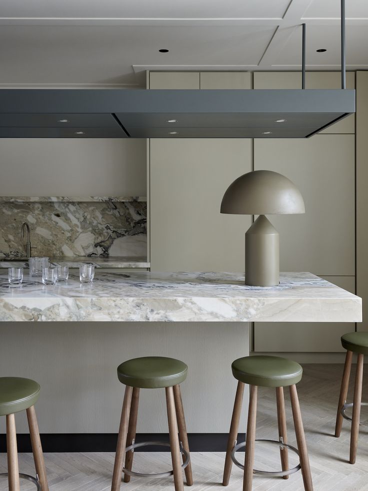 three stools in front of a kitchen island with marble counter top and pendant light