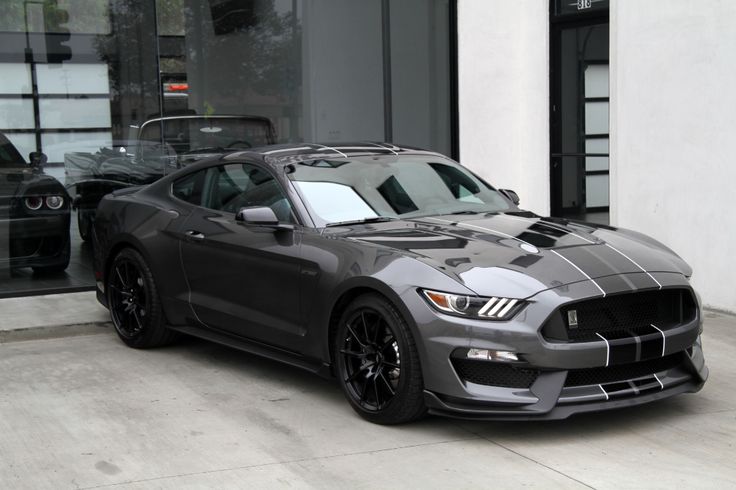 a gray mustang parked in front of a building with its hood up and lights on