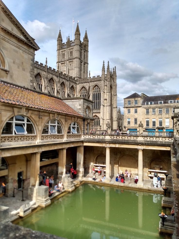 people are walking around an old building with a pond in the center and large buildings on both sides