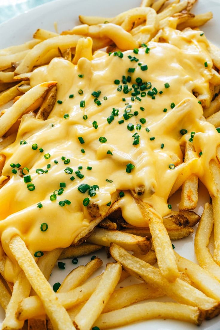 a white plate topped with cheesy fries covered in sauce and green sprinkles