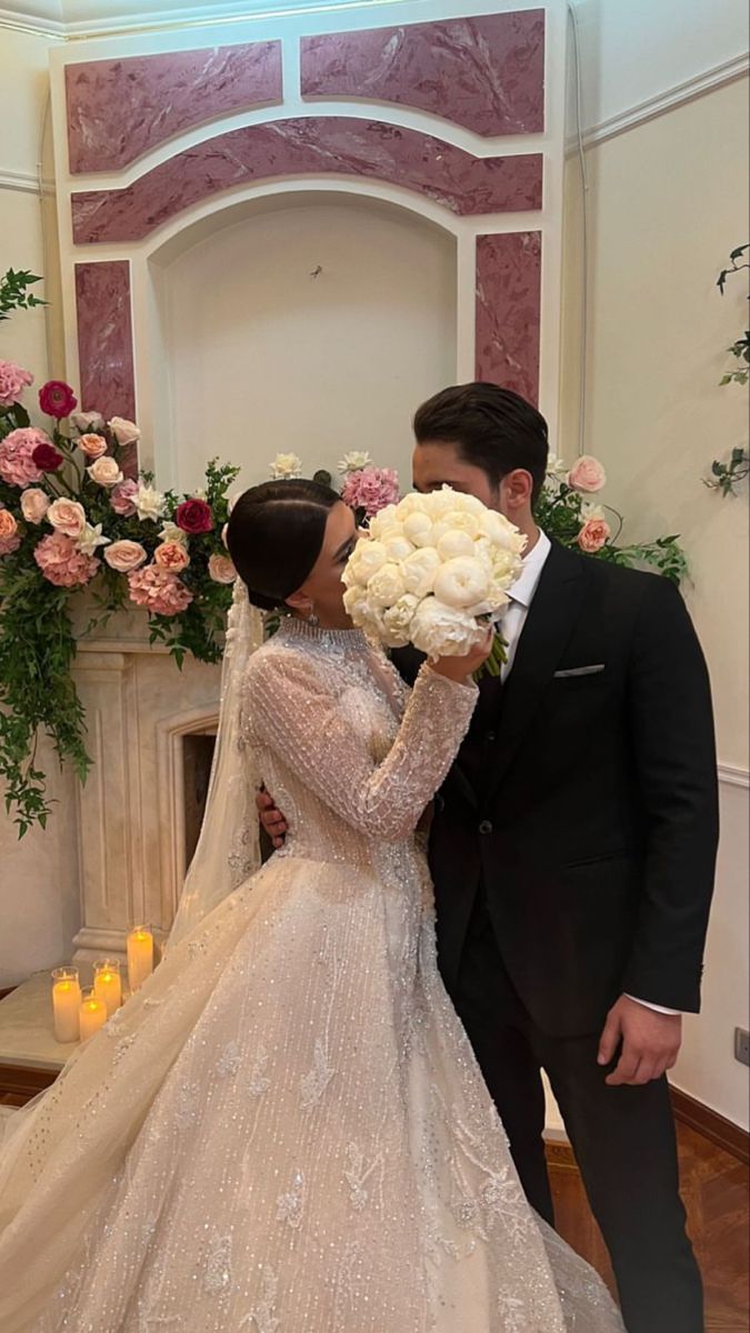 a bride and groom kissing in front of a fireplace with flowers on the mantel