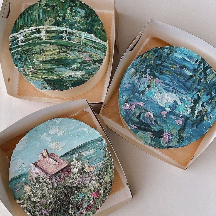 three round boxes with paintings on them sitting on a white table top, one is open and the other is closed