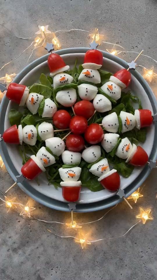 a white plate topped with tomato and mozzarella snowmen on top of lettuce