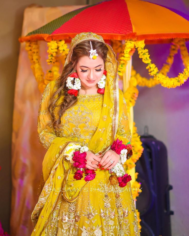 a woman dressed in yellow is standing under an umbrella with flowers on her head and veil