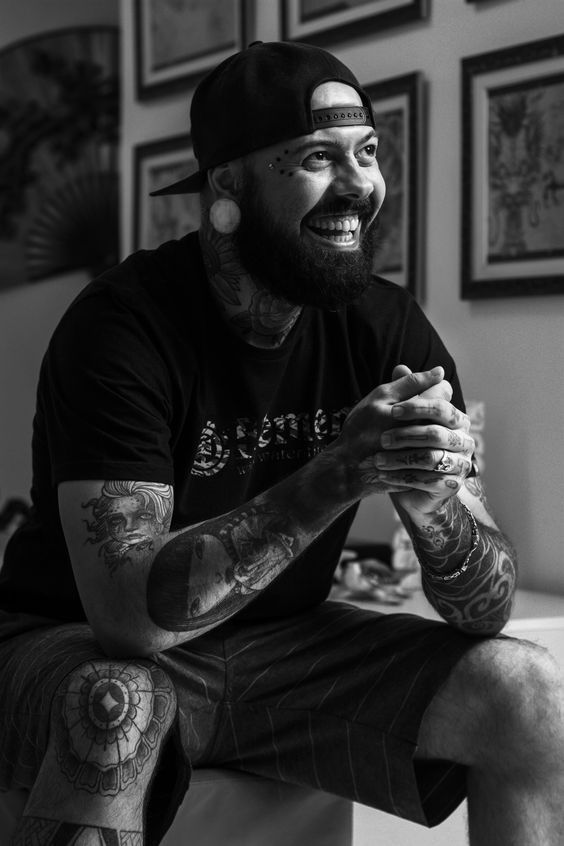 black and white photograph of a man with tattoos on his arms sitting in a living room