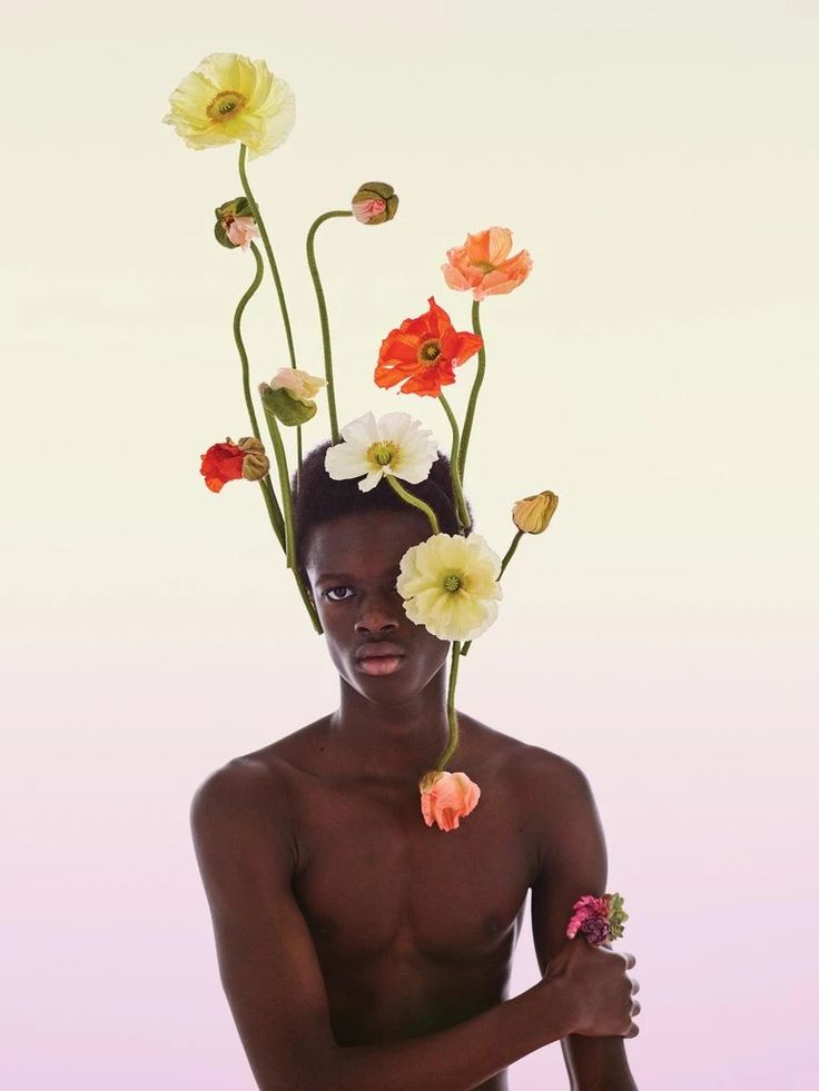 a man with flowers on his head is holding a flower in front of his face