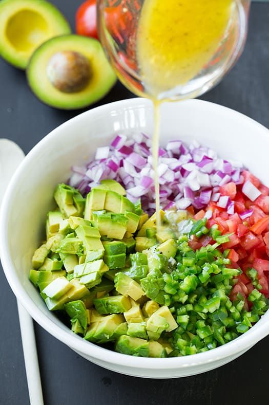 an avocado salad is being poured into a bowl with onions, red onion, and green peppers