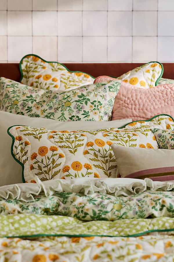 a bed topped with lots of pillows next to a white tiled wall in a bedroom