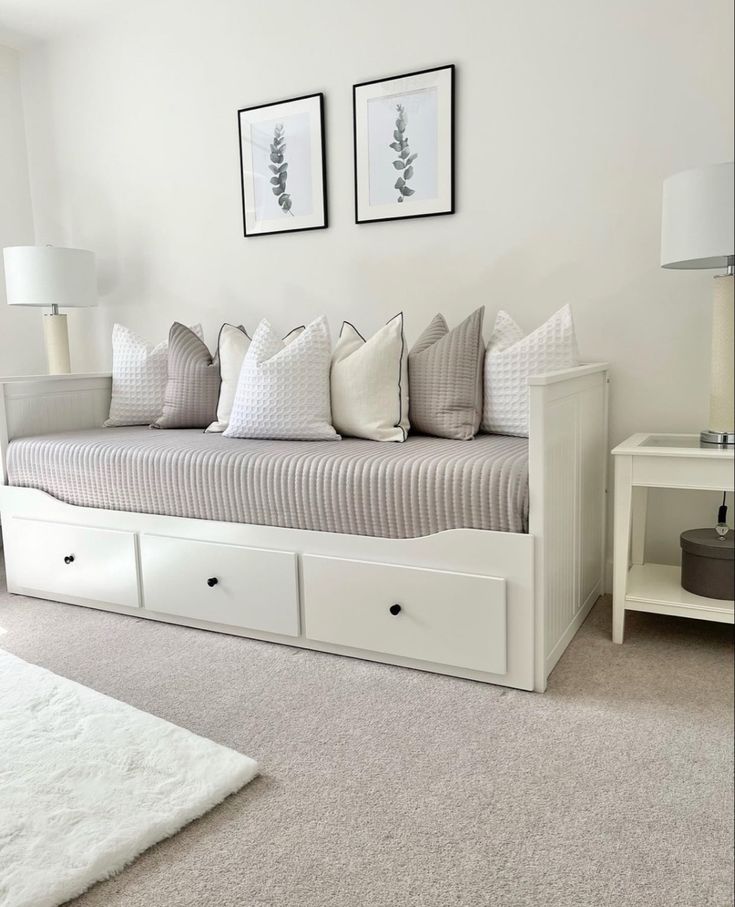 a white daybed with drawers underneath it in a living room next to a window