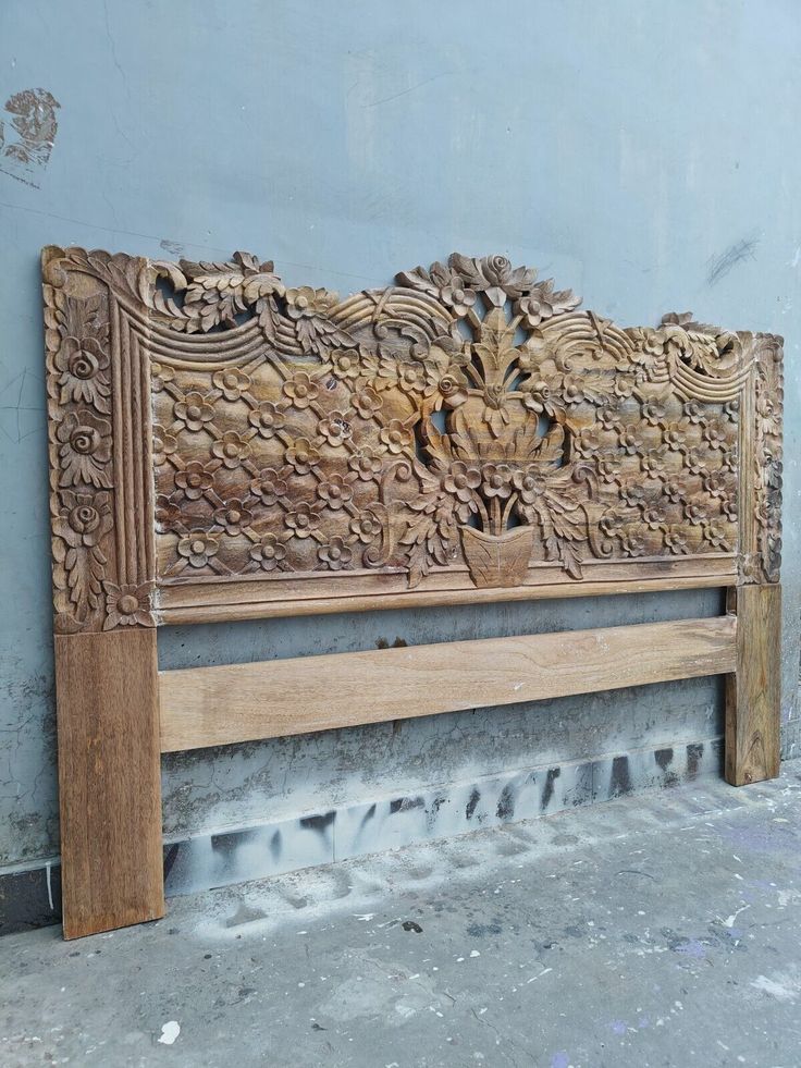 a carved wooden bench sitting on top of a cement floor next to a blue wall