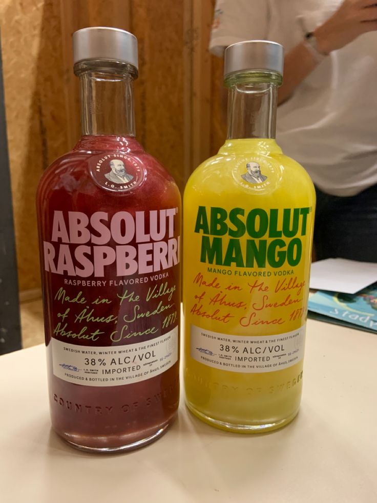 two bottles of absolut raspberry and mango juice sitting on a table