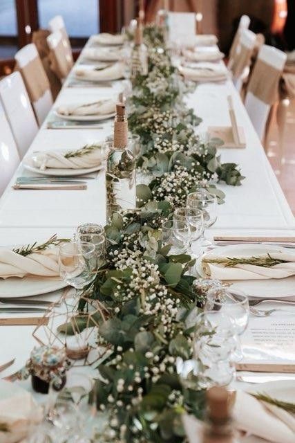 a long table with white linens and greenery is set for a formal dinner