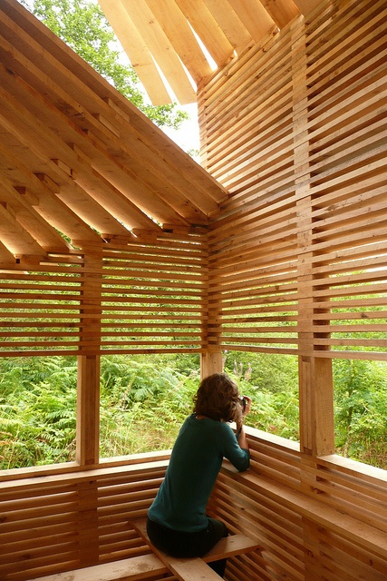 a woman sitting on top of a wooden bench in a room filled with wood slats