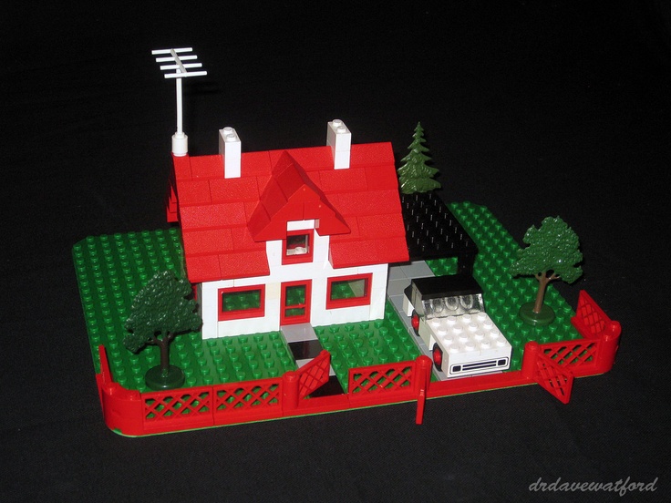 a toy house made out of legos sitting on top of a green field with trees