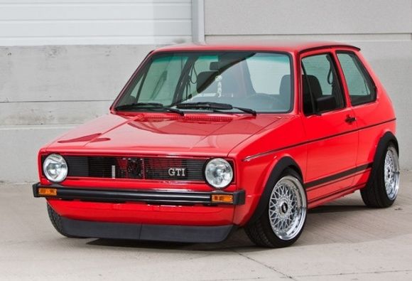 a red car is parked in front of a garage door with its hood up and windows open