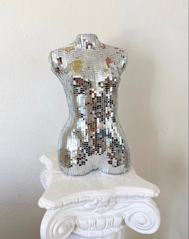 a white sculpture with silver and gold sequins on it's body sitting on top of a pedestal