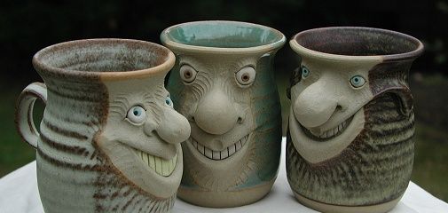 three ceramic vases with faces on them sitting on a white table cloth in front of trees