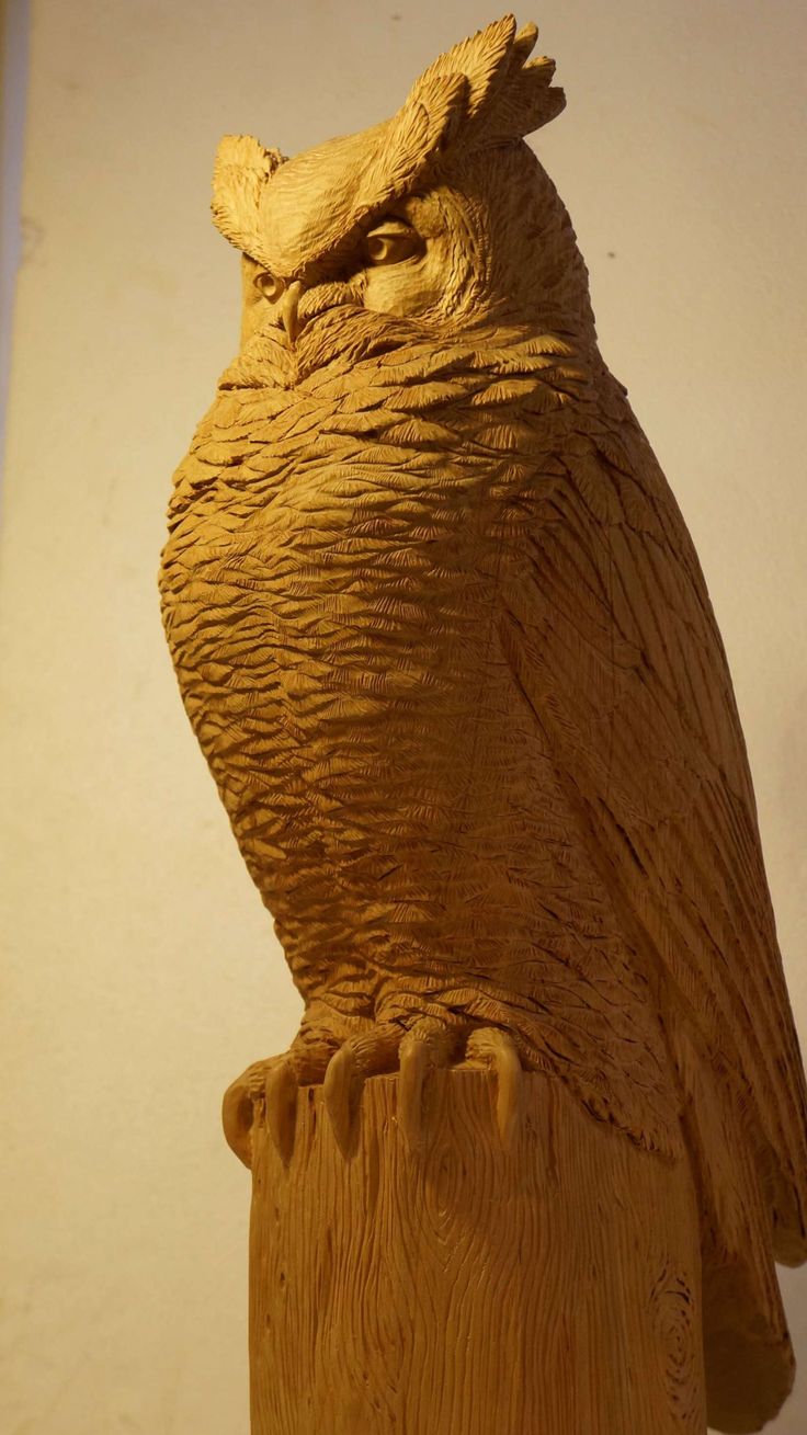 an owl statue sitting on top of a piece of wood in front of a white wall