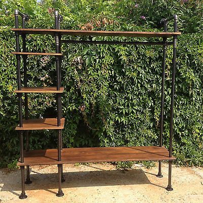 an iron and wood shelving unit in front of a bush