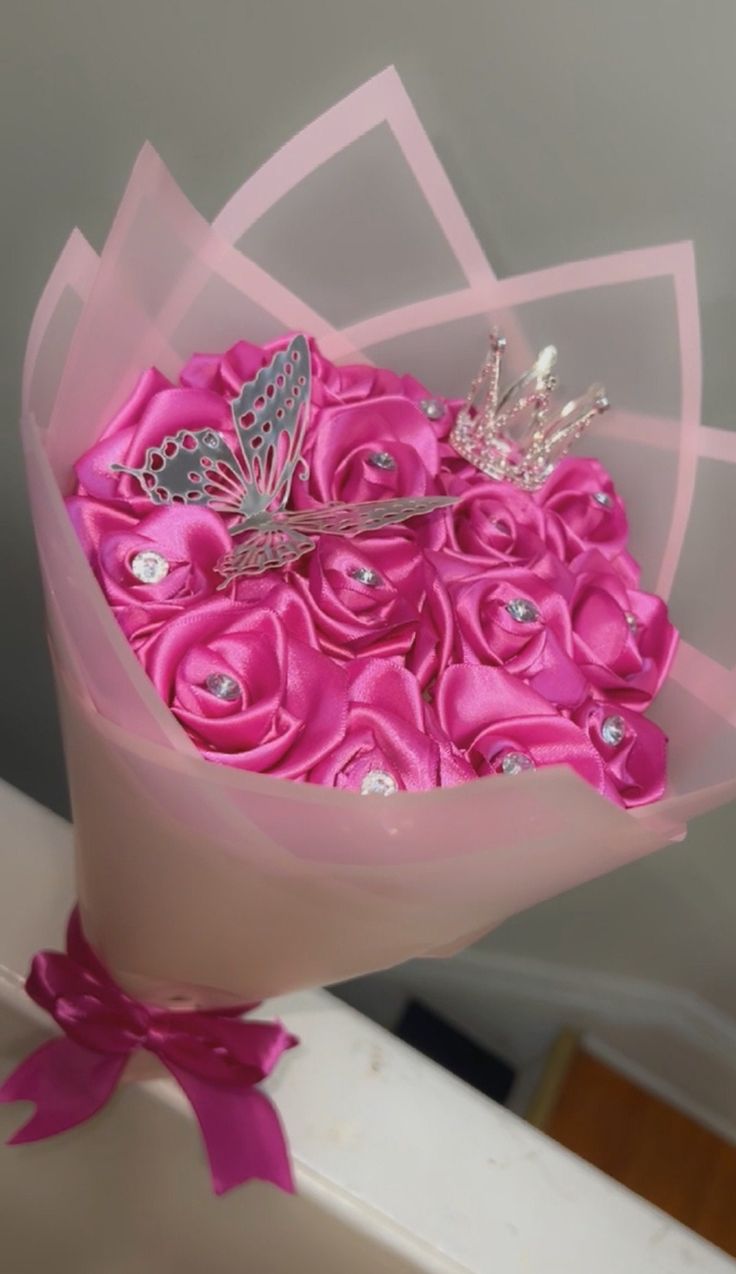 a bouquet of pink roses with a butterfly brooch in it's center, sitting on a table