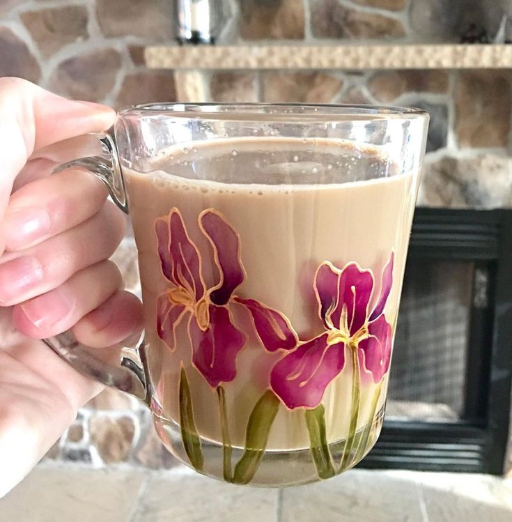 a person holding a glass mug with flowers painted on the outside and inside, in front of a fireplace