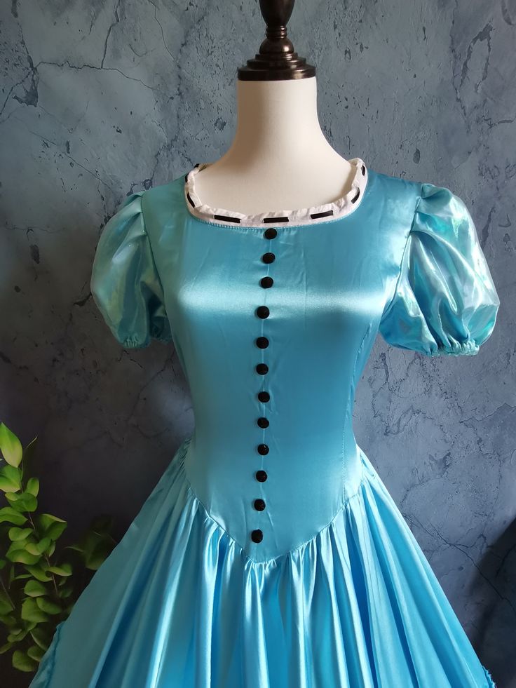 a blue dress on a mannequin with buttons down the chest and sleeves, in front of a gray wall