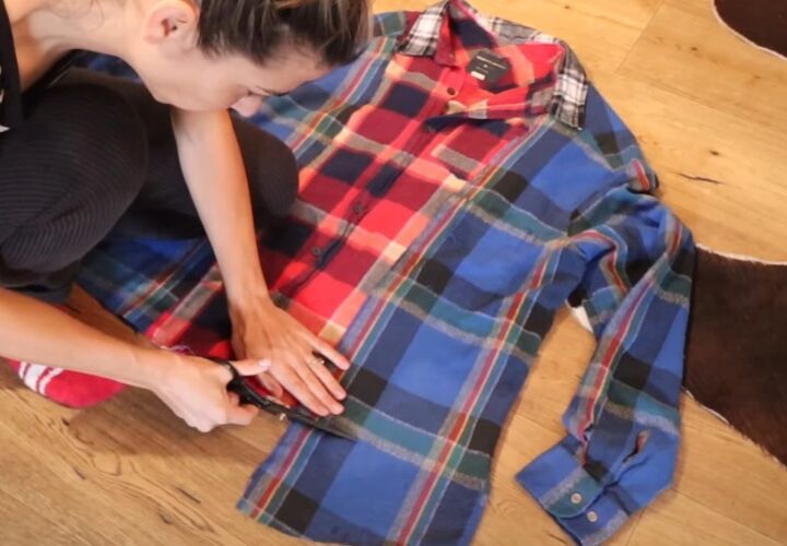 a woman sitting on the floor looking at her cell phone next to a plaid shirt