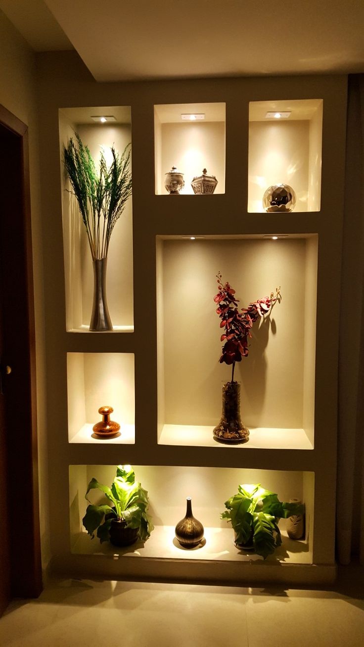 an arrangement of vases and plants on display in a wall niche with lights above them