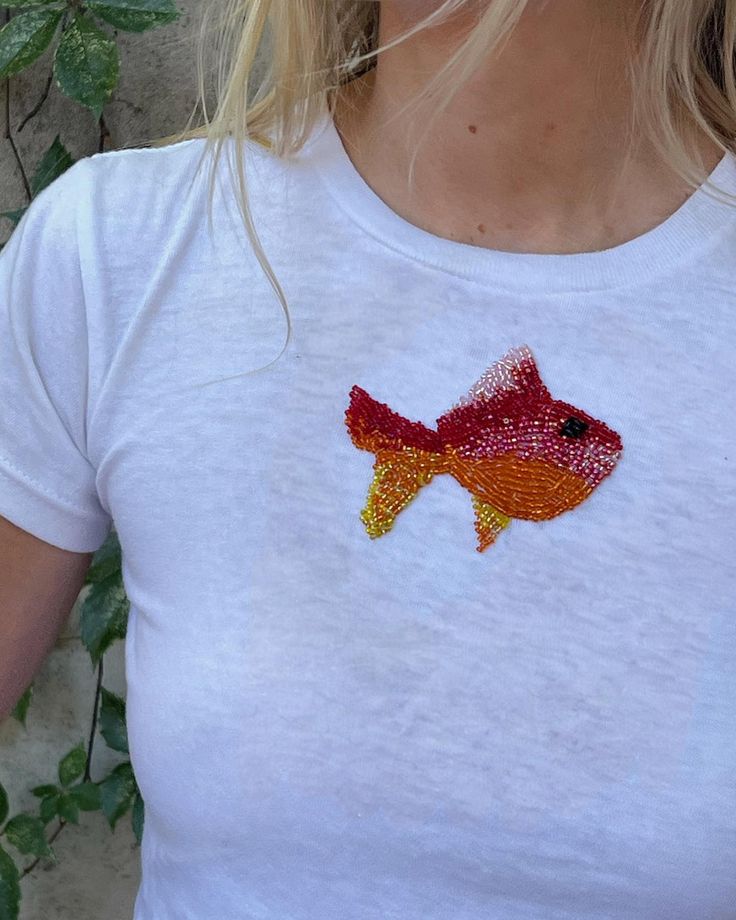 a woman wearing a white t - shirt with a fish embroidered on the back of it