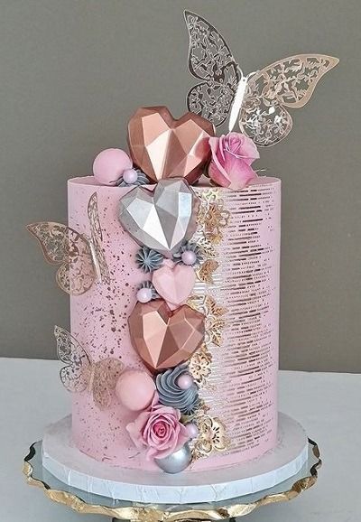 a pink and gold cake with lots of decorations on it's side, sitting on top of a table