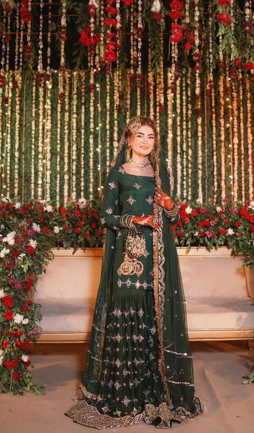 a woman in a green lehenga standing next to a floral wall with red and white flowers