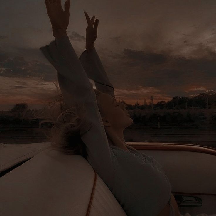 a woman sitting in the back of a car with her hands up to the sky