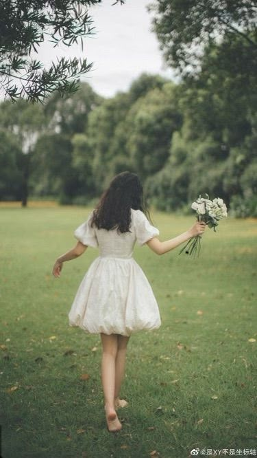 a girl in a white dress is walking through the grass with her hands behind her back