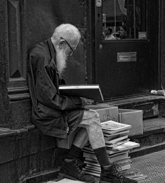 an old man is sitting on the steps with his laptop and books in front of him