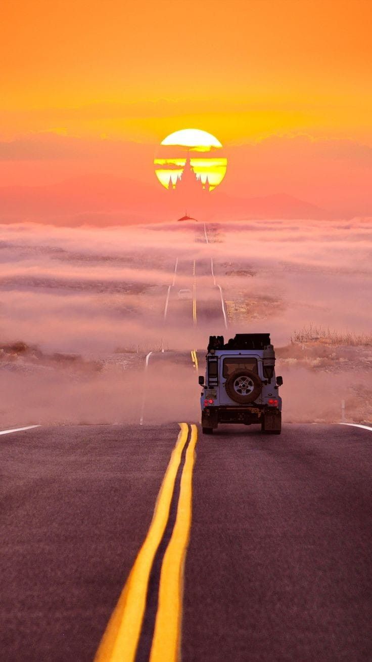 the sun is setting over the clouds and cars are driving down the road