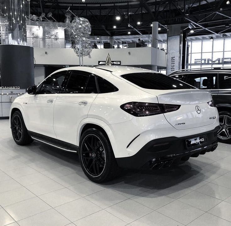 a white mercedes suv is on display in a showroom with two other cars behind it