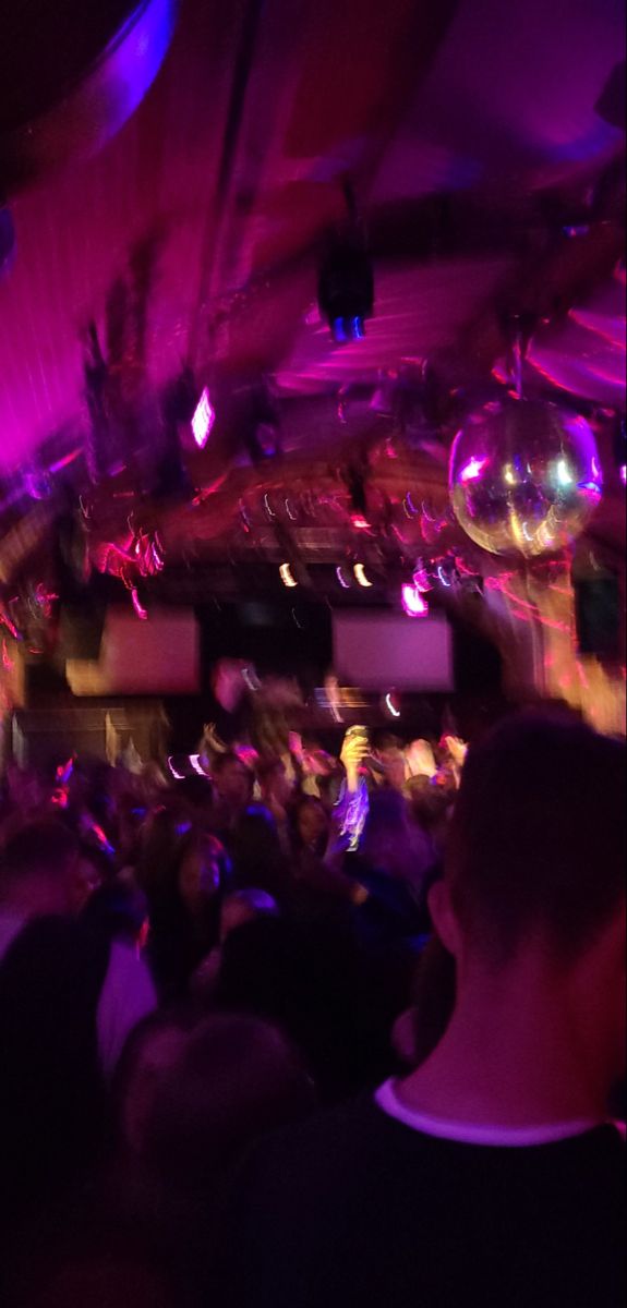 a large group of people in a room with purple lights and disco balls on the ceiling