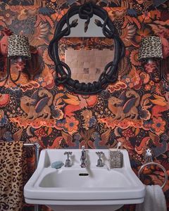 a bathroom sink sitting under a mirror next to a leopard print wallpapered wall