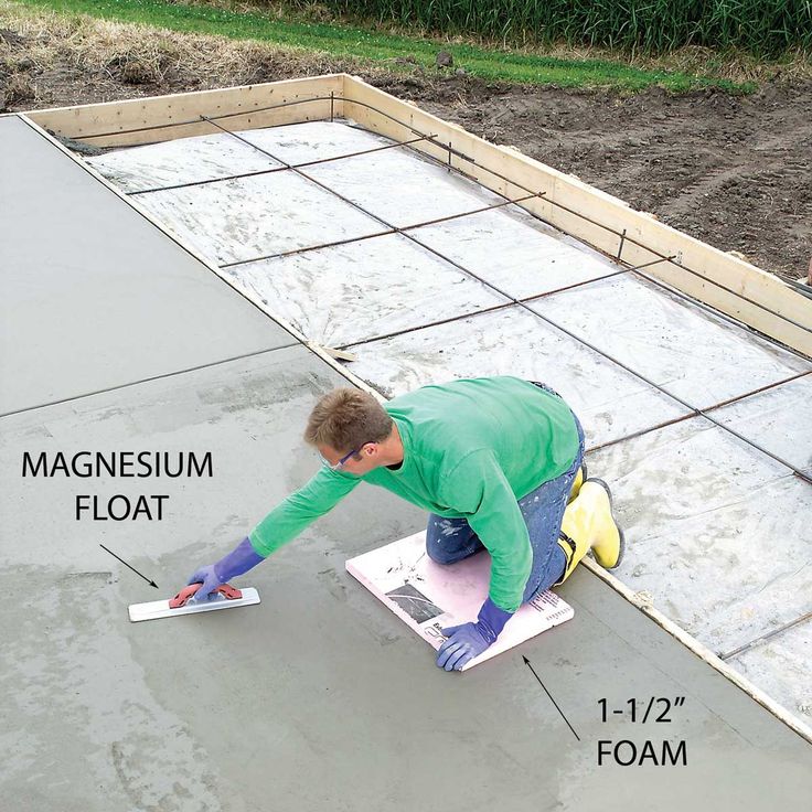 a man laying cement on top of a floor next to a garden area with plants