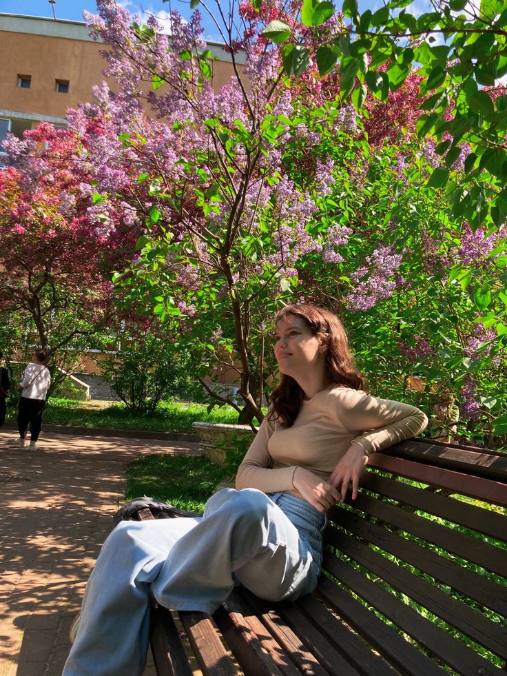 a woman sitting on top of a wooden bench next to purple and pink flowers in the park