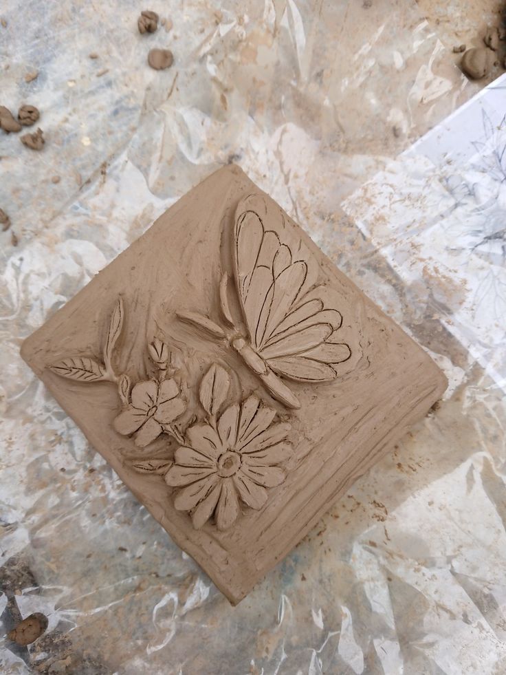 a clay sculpture of a dragonfly and flowers on a piece of tin foil with rocks in the background