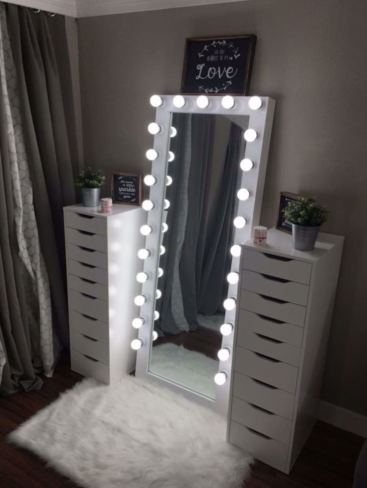 a white vanity with lights on it in a room next to a dresser and window