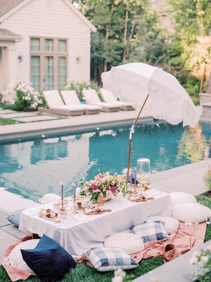 a table with an umbrella next to a pool in the grass and some food on it