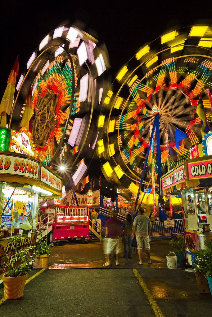 an amusement park at night with ferris wheel and carnival rides in the background as people walk by