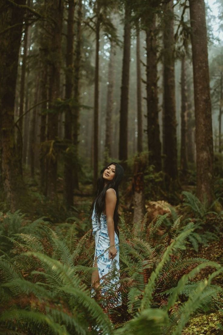 a woman standing in the middle of a forest with her eyes closed and looking up